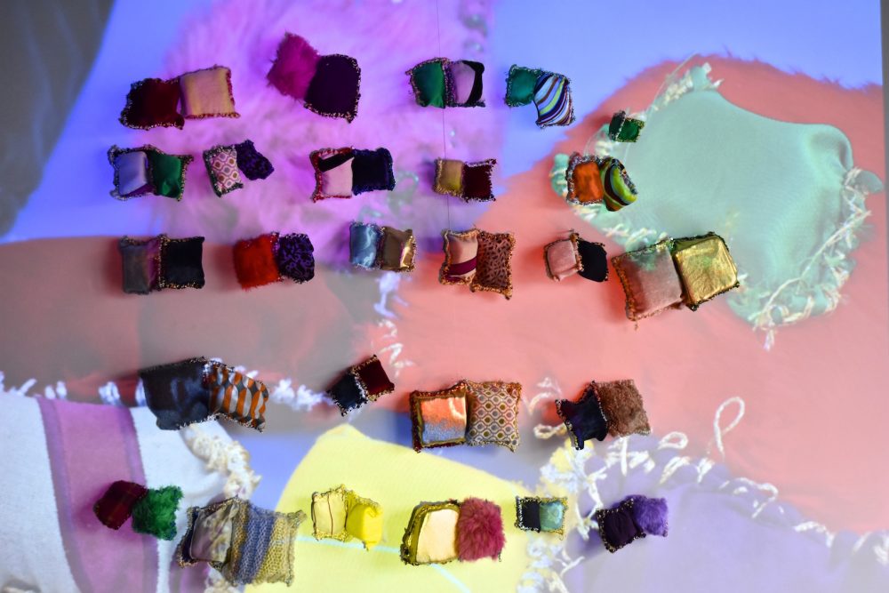 Small textile works stuck to a wall with a projection of a photograph of the work over the top