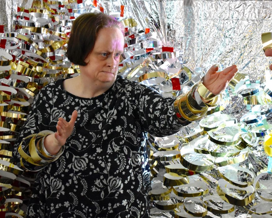 Linda Bell standing in front of her artwork made from metallic materials.