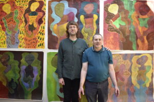 Photo of Robin Smith and Richard Pheonix standing infront of six of Robin's paintings. Both artists are looking at the camera