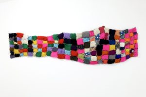 Cushioned multicoloured textile work made up of small padded rectangles stiched together.