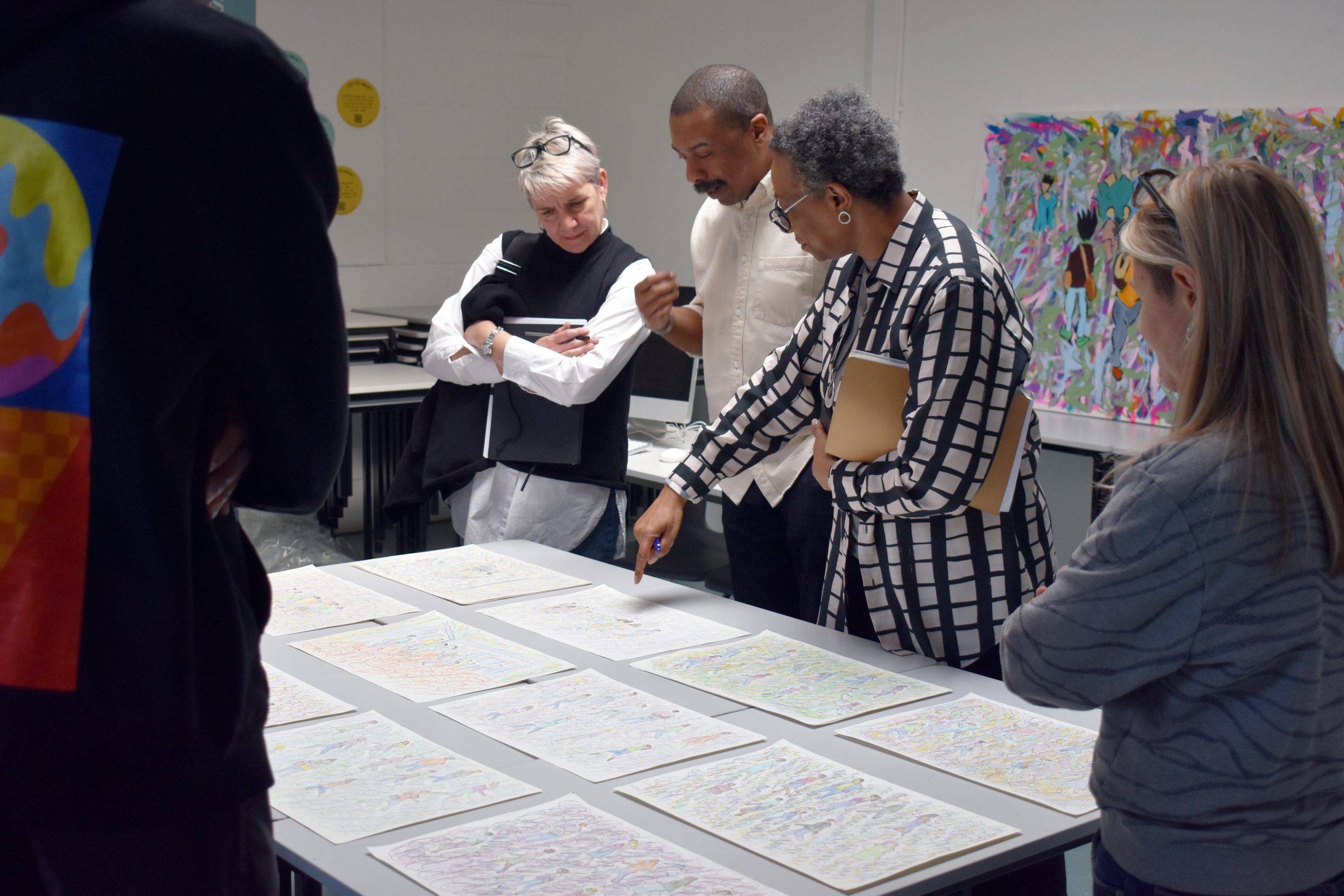 Male artist, female ActionSpace CEO and audience members look closely at abstract drawings on a table.