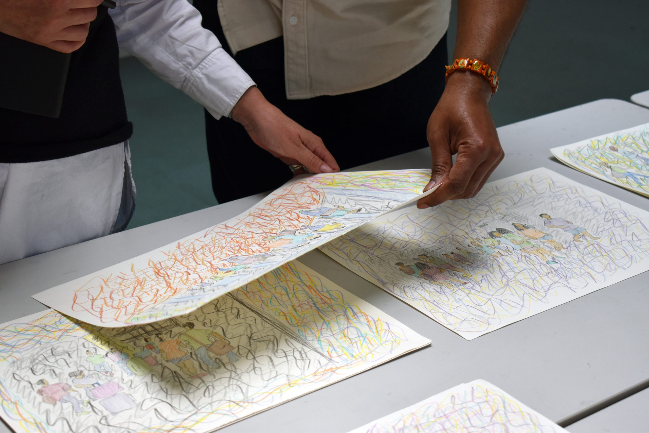 Close up image of two individual's hands holding and looking at drawings on a table.