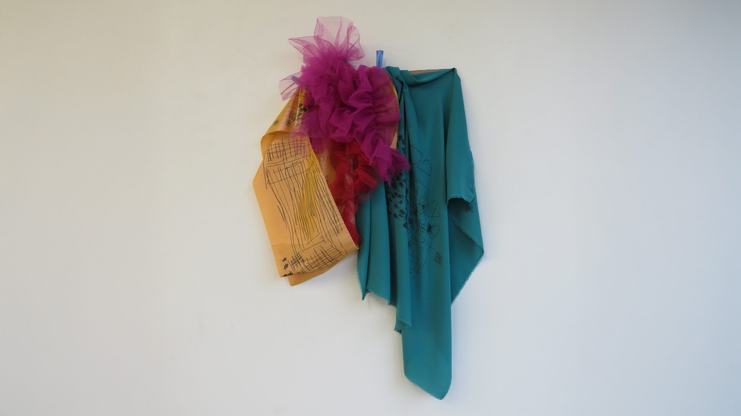 A costume hung on a white wall assembled with draping blue, yellow, pink, and red fabric. 