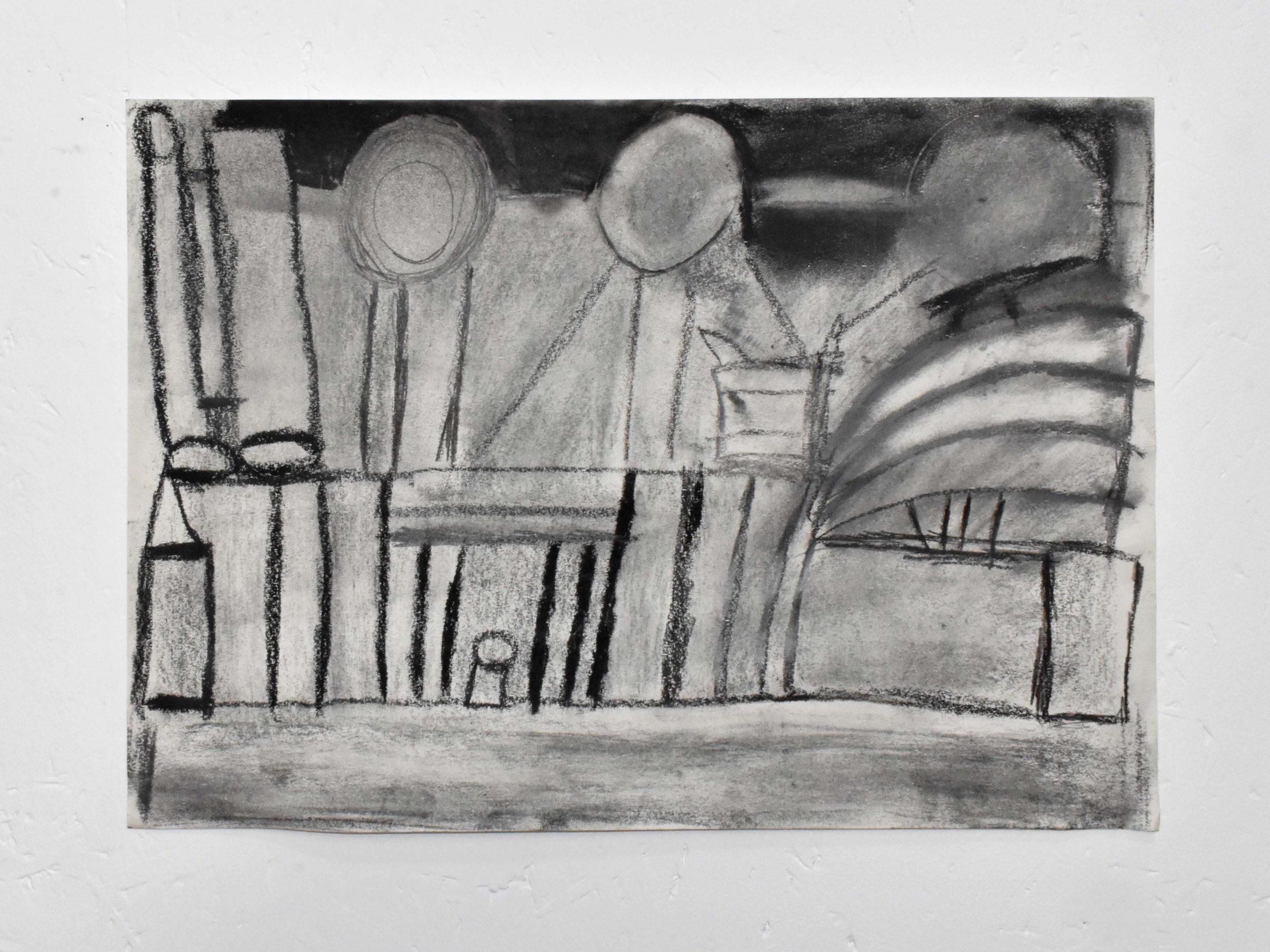 An image of a black and white, charcoal drawing on paper. Simple, abstract lines convey buildings on a street lined straight together.