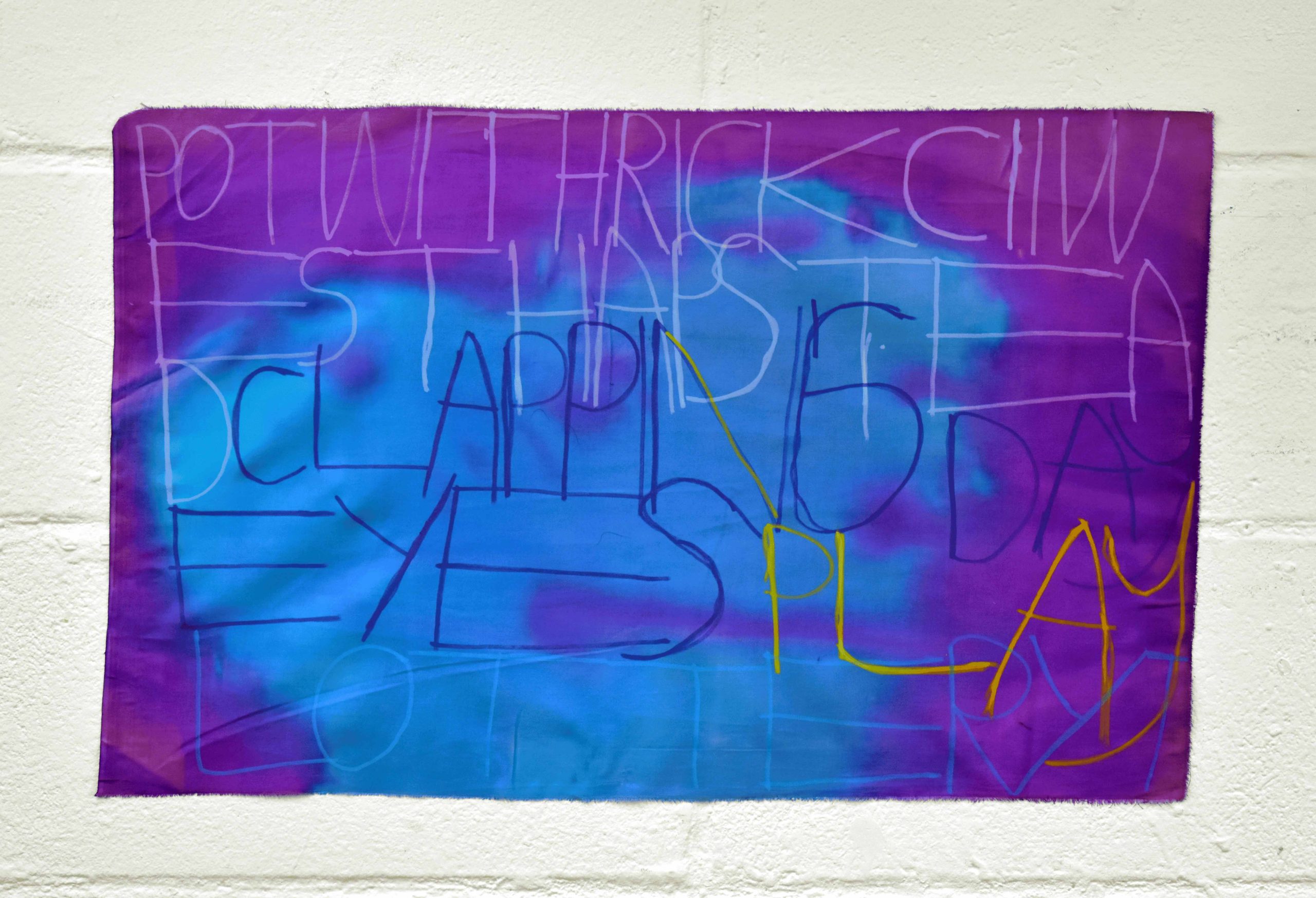 Blue ink covers centre of fabric with purple ink surrounding the corners. Layers of text in capitals are written over in marker.