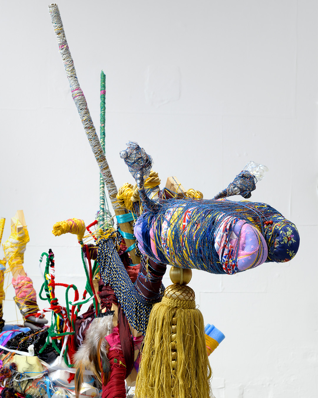 A close up of a mixed media sculpture depicting a goat's head, using thread, rope, sticks, tassels and various media wrapped together.