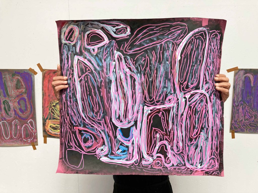 A person holds an abstract painting on paper in front of them, covering their upper body and face.