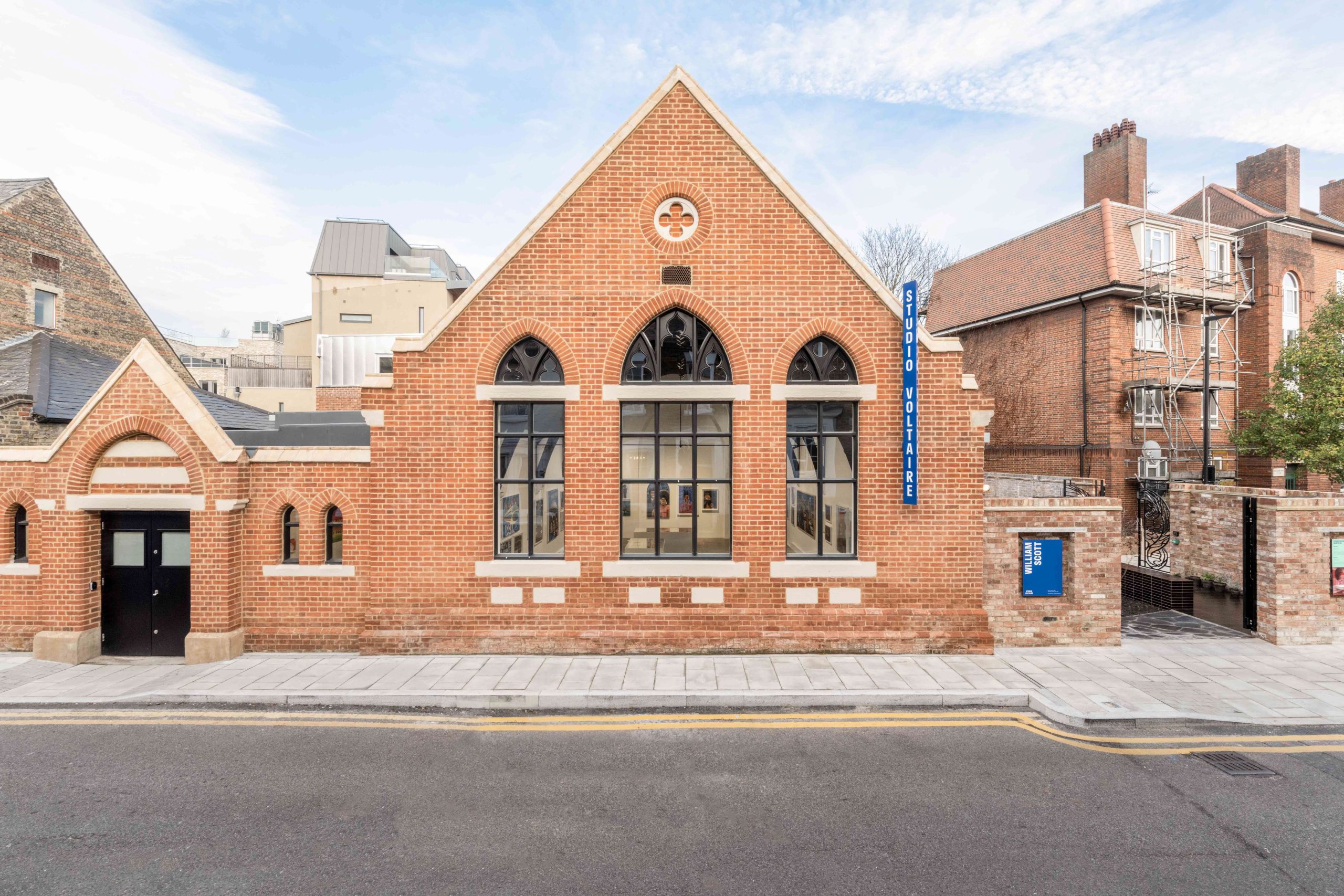 Street view of a renovated church hall artist studio and gallery space with red brick and blue skies above.