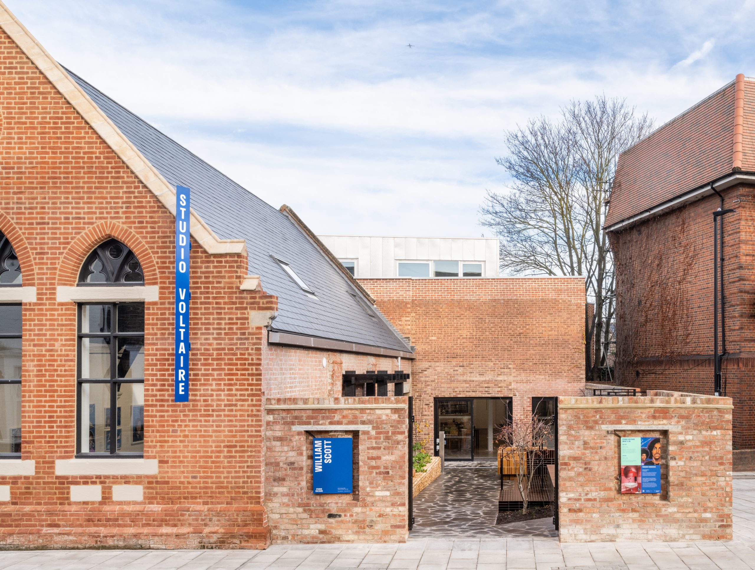 Street view of the entrance to renovated church hall artist studio and gallery space with red brick and blue signs 'Studio Voltaire'.
