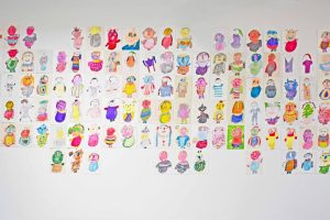 White wall covered in dozens of A4 colourful illustrations of portraits and characters