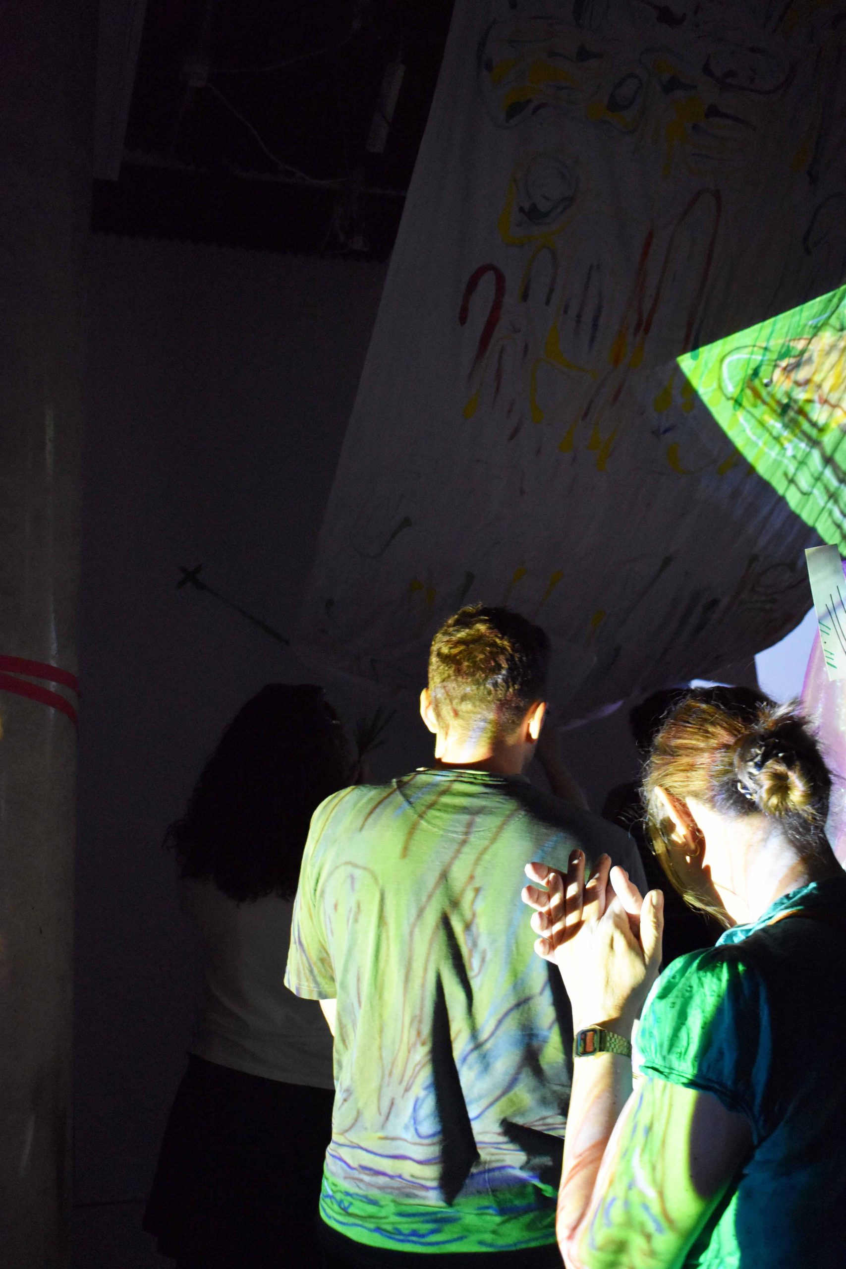 People in a line walk in the dark with colourful projections on the backs of their head.