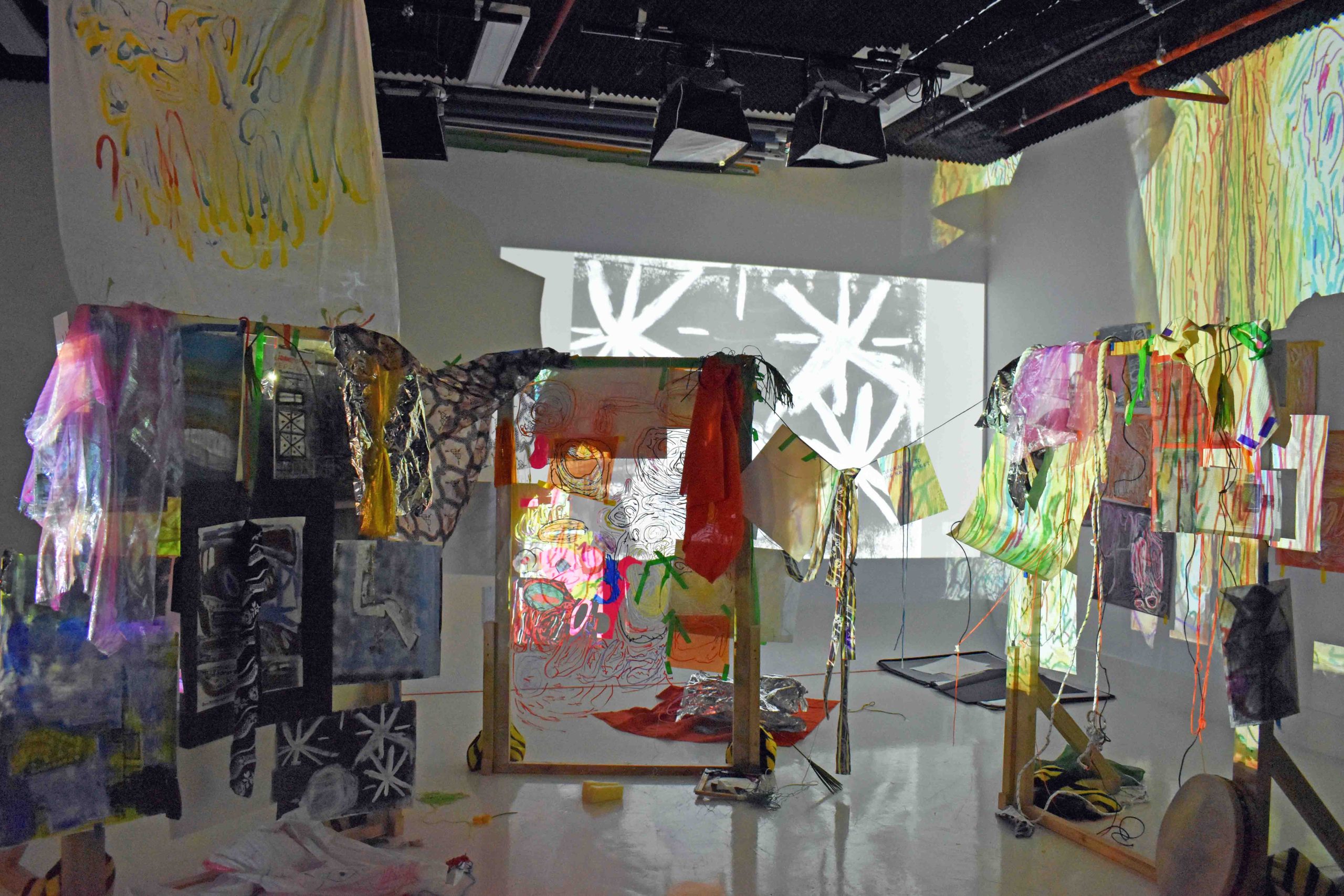 A colourful art installation in a white room with various mediums and projections.