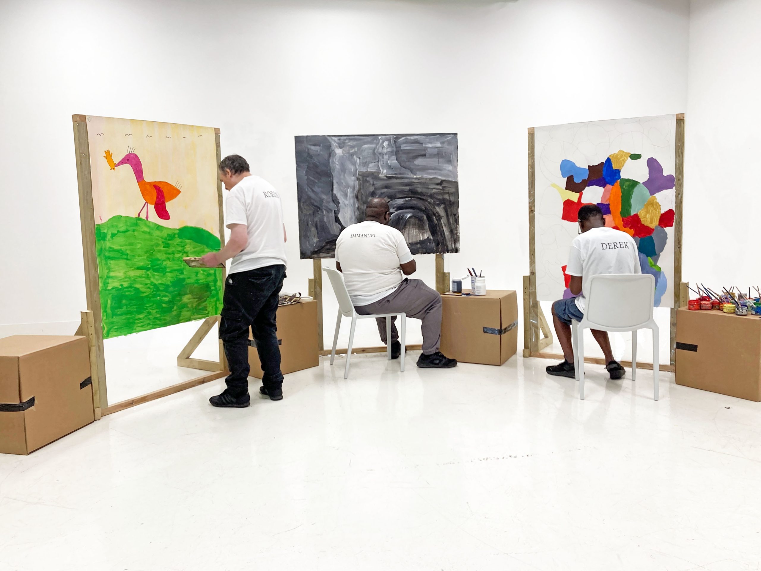 Three male artists busy painting on boards in a white space.