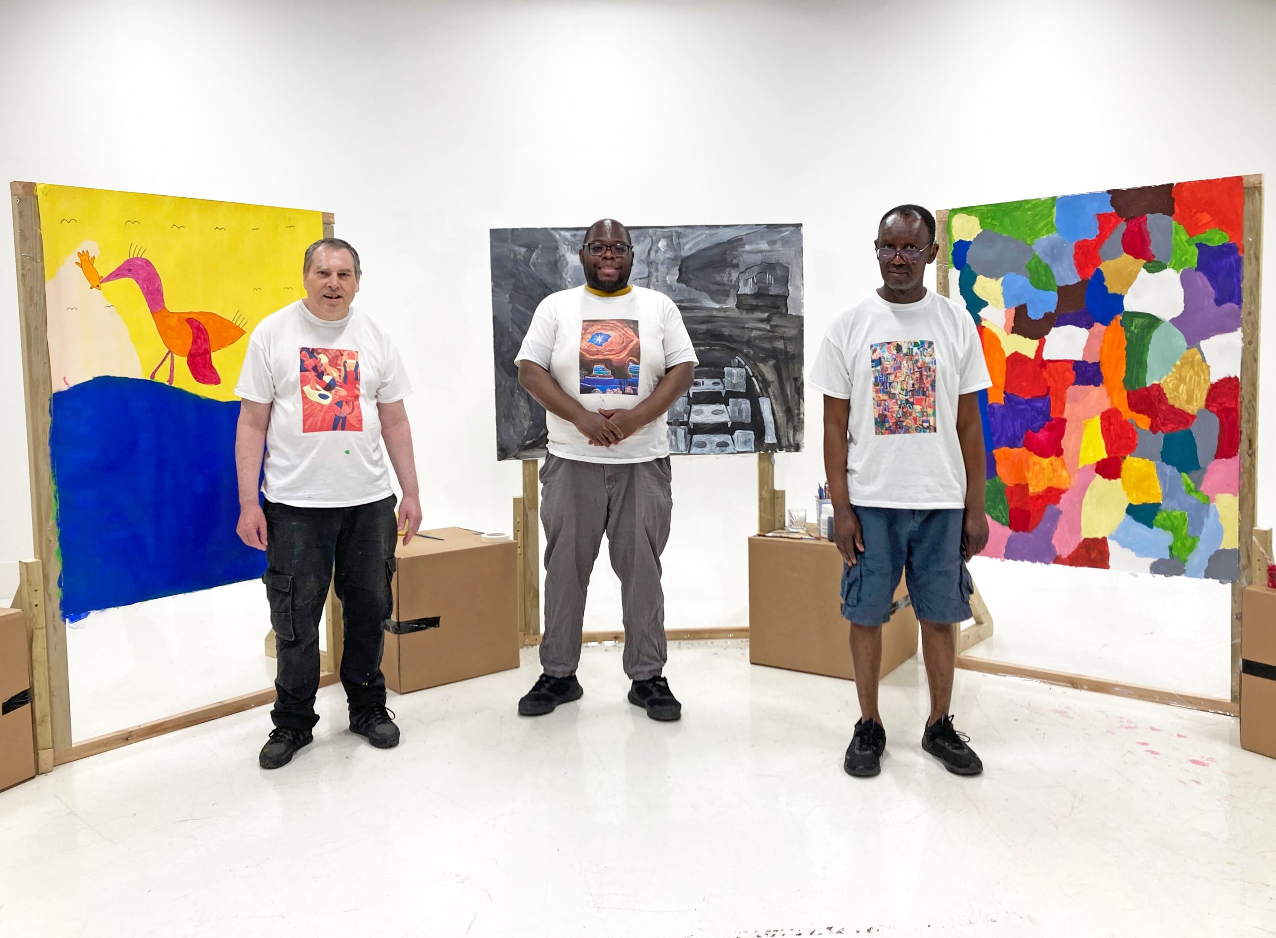 Three male artists stand for a photograph in front of their artworks.