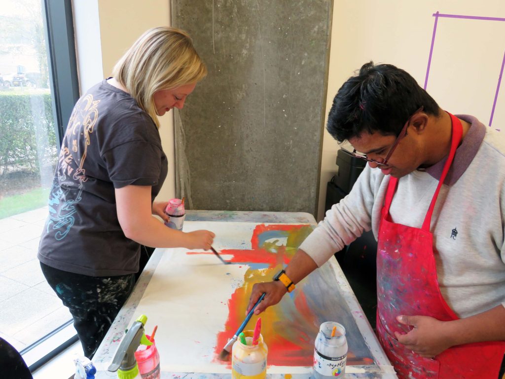 A male artist and female designer paint together in a brightly lit studio